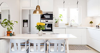 Fonctionnel et lumineux : une cuisine blanche meublée avec une table à manger, six chaises et un luminaire suspendu rond en or.