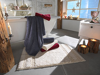 Sensation de peau douce au séchage : dans une salle de bains décorée de bougies, de grandes serviettes en éponge de différentes couleurs sont posées sur le bord de la baignoire.