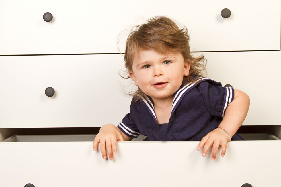 Une femme blonde et souriante est allongée avec son bébé qui joue avec un jouet à rayures rouges et blanches sur une couverture étalée par terre sur le plancher de la chambre d'enfants.