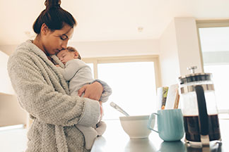 Se sentir bien chez soi : une jeune femme vêtue d'un peignoir gris douillet tient son bébé endormi dans ses bras.