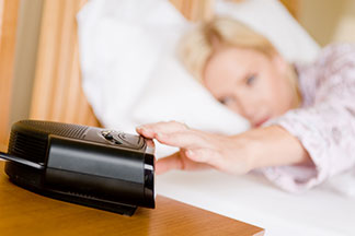 Se réveiller de bonne humeur : une femme est couchée dans son lit et éteint son radio-réveil, qui se trouve sur la table de chevet.