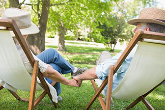 Transat au lieu de chaise longue : un couple de personnes âgées est assis côte à côte sur deux transats dans le jardin, se tenant la main.