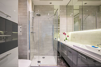 Un miroir de salle de bains rectangulaire avec éclairage intégré est suspendu au-dessus d'un meuble sous vasque avec deux lavabos rectangulaires.