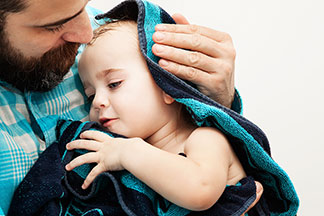 Un label de qualité crée de la confiance : un père tient son bébé dans ses bras, enveloppé dans une serviette bleue.