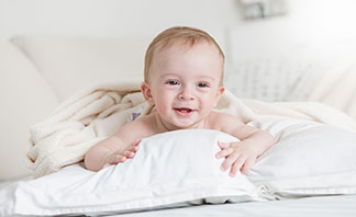 La bonne qualité pour vos taies d'oreiller : un enfant rieur est allongé sur le ventre sur un oreiller blanc dans son lit.