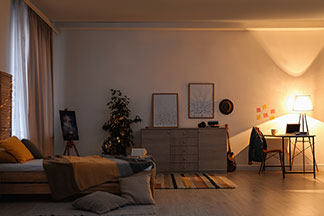 Une bonne qualité pour un bon éclairage : une chambre à coucher contenant un lit, une commode et une table, baignée de la lumière jaune chaude d'une lampe de table.
