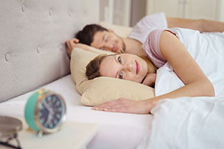 Se réveiller en toute détente : une jeune femme est allongée dans son lit avec un homme endormi à ses côtés et un réveil sur la table de chevet.