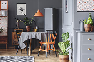 Au milieu de la salle se trouve une table ronde avec une nappe carrée de couleur anthracite comme contraste. La lampe orange et une chaise de la même couleur sont d'autres éléments de style.