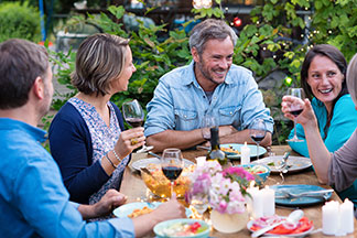 Meubles de jardin et de balcon pour passer des heures ensemble : six adultes sont assis sur la terrasse à la table à manger et discutent de manière animée. Il y a de la vaisselle et des verres sur la table.