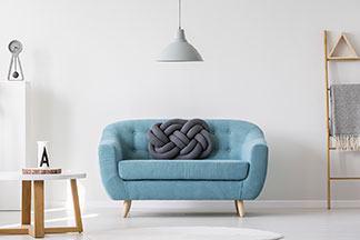 Au milieu de la pièce se trouve un canapé de couleur turquoise, au-dessus duquel est suspendu un plafonnier gris – sur le côté gauche de la pièce se trouve une table basse ronde avec un plateau blanc, sur le mur du fond des étagères en forme d'échelle.