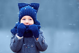Un petit garçon avec un sac à dos, un imperméable et une casquette tend joyeusement ses mains dans des gants de coton aux couleurs de l'arc-en-ciel vers la caméra.