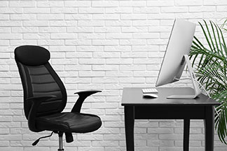 Chaise noire devant un bureau, également noir, sur lequel est placé un ordinateur.