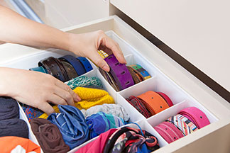 Accessoires de rangement pour le tiroir : gros plan des mains d'une femme rangeant une ceinture dans un tiroir, qui est structuré par un système d'organisation.
