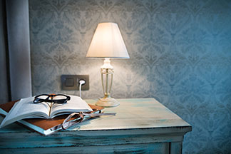 Un design chic pour votre lampe : une lampe de table avec un abat-jour blanc est posée sur une table d'aspect vintage sur laquelle reposent un classeur, un livre ouvert et une paire de lunettes.