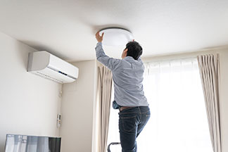 Plafonnier pour les pièces basses : un homme en blue-jeans et en chemise est debout sur une échelle, sur le point d'installer une lampe assiette au plafond.