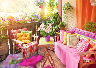 Décoration de jardin pour le balcon : sur un balcon, il y a un banc en bois et une chaise en bois décorée de coussins colorés et une petite table. Des pots de fleurs avec des plantes sont suspendus à la balustrade.