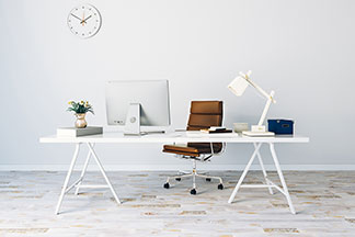 Une chaise de bureau marron se trouve derrière un bureau blanc avec un ordinateur, une lampe et des étagères.