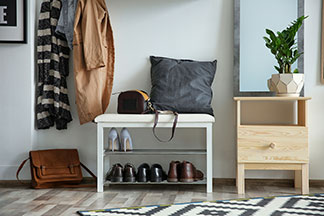 Pratique et décoratif : un banc blanc chaussures se trouve dans un couloir avec un miroir, des vestes suspendues sur un portemanteau et un tapis.