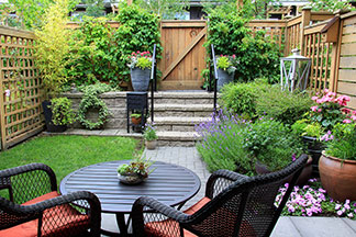 Meubles de jardin de bonne qualité: sur une petite terrasse dans un jardin se trouvent deux chaises de jardin sombres avec des coussins et des dossiers rouges et une table.