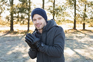 Vos casquettes et gants pour hommes dans une qualité incroyable : un jeune homme porte un bonnet bleu en laine sur la tête, a les mains gantées posées dessus, et sourit à l’objectif.