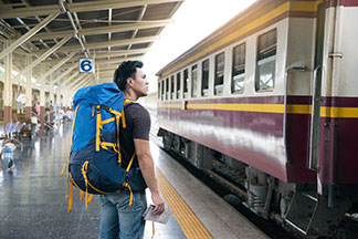 Valises et accessoires de voyage pour hommes ou sac à dos ? Sur un quai de gare, un jeune homme est en train de regarder le train devant lui, en tenant une carte à la main.