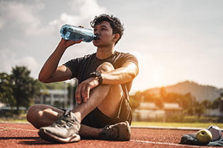 Socquettes pour hommes : un jeune homme est assis sur un terrain de sport et boit de l'eau.