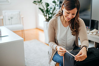 Dans son salon, une jeune femme est en train de mesure sa valise pour femmes.
