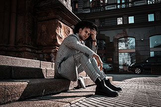 Des bottes pour hommes pour un look professionnel : un jeune homme portant des bottes noires, un pantalon de costume à carreaux, une veste à carreaux assortie ainsi qu'un chapeau est assis à l'extérieur, sur un escalier en pierres.