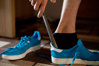 Gros plan sur des socquettes pour hommes : la jambe d'un homme portant des socquettes noires, en train d'enfiler une basket bleue à l'aide d'une chausse pied.