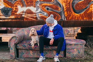 Socquettes pour hommes au coloris vif : un jeune homme est assis à l’extérieur sur un canapé et porte des chaussettes bleues assorties à sa veste. Son chien est assis à côté de lui.