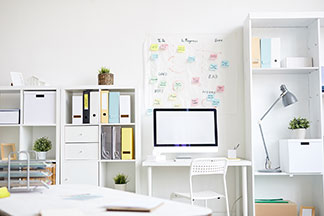 Un bureau bien organisé : un bureau blanc équipé ainsi qu’un bureau placé entre deux étagères sur lequel sont disposés des classeurs et des boîtes de rangement.