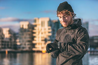 Casquettes et gants pour les hommes pour le sport : un jeune homme s'apprête à faire son jogging, il porte un bonnet noir, des vêtements de sport ainsi que des gants pour hommes en matière polaire et est en train de regarder sa montre.