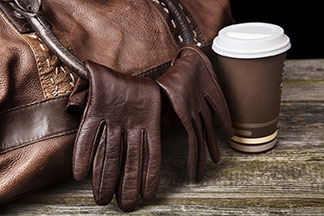 Gros plan sur des gants en cuir marron pour hommes, suspendus à la anse d'un sac de voyage en cuir marron.