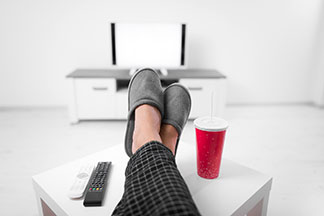 Les chaussons pour hommes sont synonymes de confort : un homme dont on voit juste les jambes posées sur une table basse est assis sur son canapé. Il porte des pantoufles.