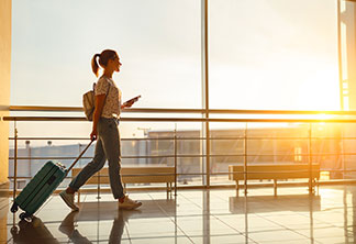 Une jeune femme marche devant une baie vitrée d’aéroport avec sa valise pour femmes à l'aéroport.