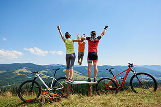 Un homme et une femme en tenue de cyclistes, dans un point d'observation, dos à la caméra, se tiennent la main debout avec leur enfant entre eux et le soulèvent.