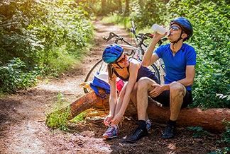 Un jeune couple portant des vêtements de vélo courts et un casque de vélo s'assoit sur un tronc d'arbre et fait une pause dans la forêt pendant une promenade à vélo.