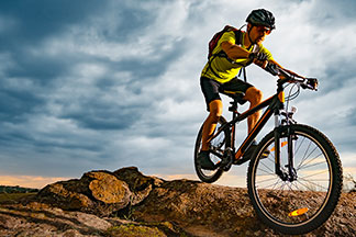 Un jeune homme portant un maillot de cycliste à manches courtes et un short de cycliste comme vêtement de vélo fait du VTT dans les montagnes.