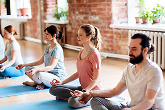 Les bons vêtements de yoga : un groupe de jeunes gens sont assis en rangée et méditent sur leurs tapis de yoga.