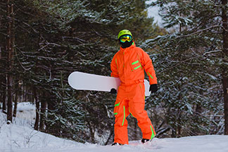 Un snowboarder portant une combinaison de ski orange s'aventure hors-piste dans une forêt enneigée en hiver.