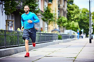 Le bon pantalon hommes pour le sport : un homme barbu en chemise à manches longues et en pantalon de sport fait son jogging dans une ville.