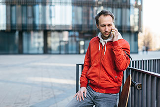 Veste de sport pour un usage quotidien : un jeune homme portant une veste de sport rouge et un longboard parle sur son smartphone.