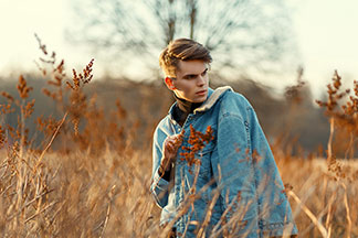 Veste pour les loisirs : un jeune homme traverse un champ automnal dans l'ambiance du soir, vêtu de sa veste en denim avec un col en laine blanche sur l'épaule.