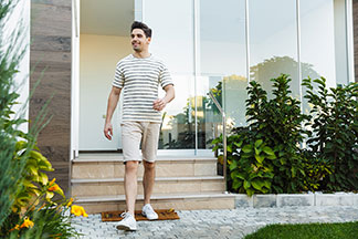 Un jeune homme en haut à rayures noires et blanches et en short de chino beige quitte sa maison ravi.
