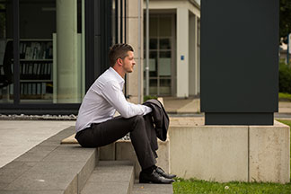 Pantalons hommes pour le bureau : un homme en chemise blanche et pantalon en tissu anthracite est assis sur un escalier de pierre. Il tient la veste assortie dans sa main.