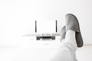 Chaussures hommes pour la maison : gros plan sur les jambes d'un homme étendu sur une table. Sur ses pieds, le monsieur porte des pantoufles.