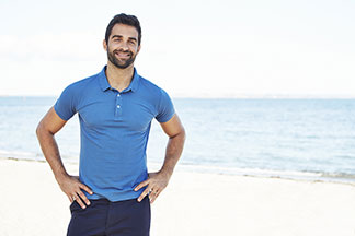 t-shirt de sport pour tous les jours : un homme barbu en polo bleu clair sourit joyeusement à la caméra sur une plage.