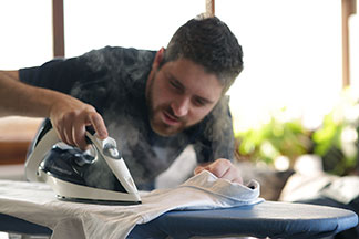Un homme repasse sa chemise manches longues.