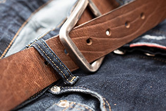 Des accessoires hommes qui attirent l'attention : gros plan d'une ceinture en cuir marron sur un jean.