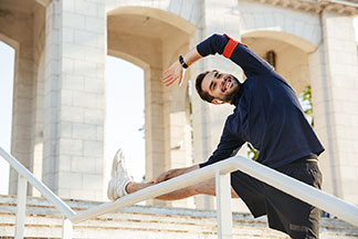 Un jeune homme barbu en t-shirt de sport manches longues fait des exercices d'étirement sur une rampe d'un bâtiment historique.